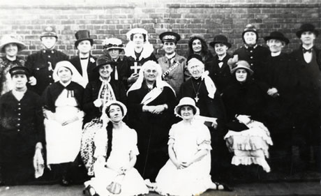 Photograph showing nineteen women in costume posed in front of a brick wall; they are dressed as policemen, nurses, clergymen, gentlemen, old ladies and, possibly, Queen Victoria; in addition, a zoo keeper and ladies in elaborate frocks form part of the group; they have been identified as the members of the cast of the South hetton Mothers' Union play in the 1930s