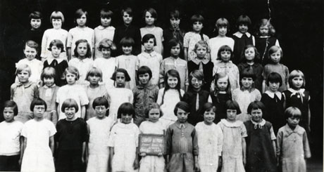 Photograph of forty five girls aged approximately nine years lined up in a group; a girl on the front row is holding a notice reading; South Hetton Council Girls' School Class 4 1929