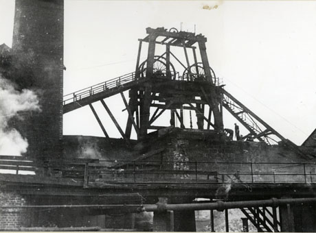 Photograph showing a walkway and part of a chimney with a close-up of the winding gear of a colliery, which has been identified as South Hetton Colliery