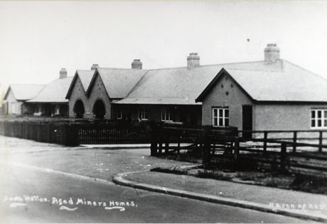 Postcard photograph entitled South Hetton Aged Miners Homes. Haven of Rest, showing the exterior of the front of a block of single-storey houses with gardens in front of them
