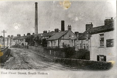 Postcard photograph entitled East Front Street, South Hetton, showing a road running away from the camera; the right side of the picture shows half of the facade of the Grey Horse Inn and houses lining the road; behind the houses a tall chimney can be seen