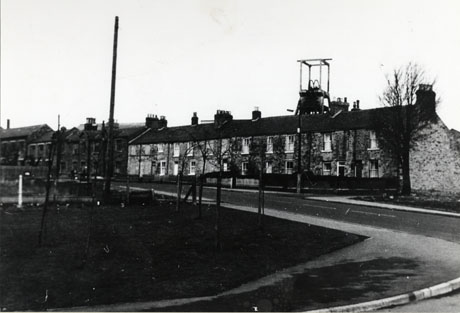 Photograph showing, in the foreground, a piece of open ground and a road running away from the camera; on the side of the road are a terrace of houses leading to a large imposing building; immediately over the roof of the terrace, the top of the winding gear of a colliery can be seen; the photograph has ben identified as The Old Granary, South View, South Hetton