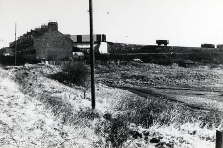 Photograph showing open ground with a dusting of snow on it; in the distance, at the left of the picture, the end of a terrace of houses can be seen; on the right, a coal waggon on a railway on an embankment can be seen outlined against the sky; the terrace has been identified as Railway Terrace, South Hetton