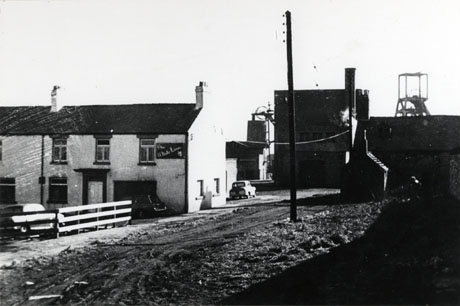 Photograph showing, on the left of the picture, an end-of-terrace house with a sign reading The White Lion; behind the White Lion are what may be colliery buildings and the top of the winding gear of the colliery; the colliery has been identified as South Hetton