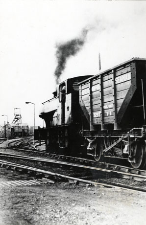 Photograph showing rails running away from the camera towards the buildings and winding gear of a colliery; on the rails is a locomotive pulling a coal waggon, seen from the side; the coal waggon has the name Seaham on it; the locomotive has been identified as Engine 62 at South Hetton Colliery, 1972