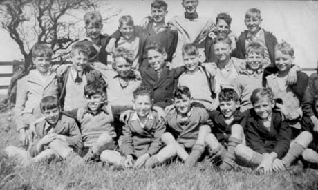 Photograph of twenty two boys aged approximately twelve years seated on the ground in a field with a tree behind them; they are dressed in jackets, jumpers, shorts and long socks; they have been described as Boys at Cresswell Camp; they have been identified as being natives of South Hetton