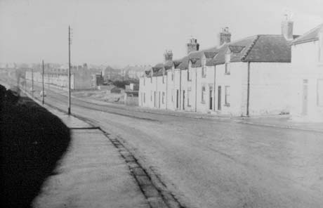 Photograph of a street running away from the camera, showing a terrace of seven houses in the foreground on the right of the street; in the distance on the same side further terraces can be seen; a patch of open ground is between the terraces; cars can be seen in the distance driving away from the camera; the street has been identified as Front Street, South Hetton