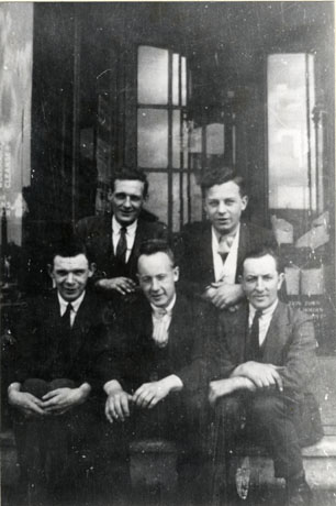 Photograph of five men sitting on the steps of possibly the entrance to a large building; they are wearing suits and ties; they have ben identified as employees of the Station Town Co-operative Society