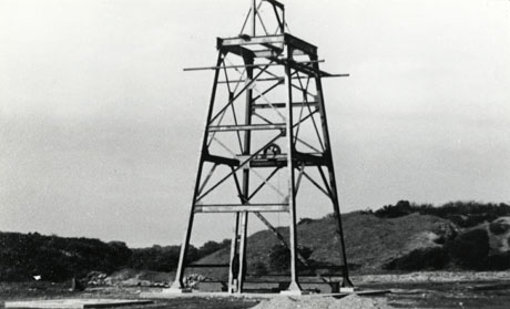 Photograph showing a tall metal square framework, the superstructure aboveground of The Marley Pumping Shaft, Station Town Pit, July 1952; behind the superstructure low hills can be seen
