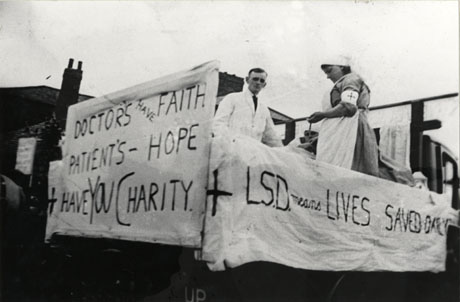 Photograph showing the back of a motor lorry decorated for a carnival, identified as being in Thornley; on the lorry are man in a white coat, a woman in nurse's uniform and a patient; at the back is a sign reading: Doctors Have Faith Patients Hope Have You Charity?; at the side another notice reads: L. S. D. Means Lives Saved Daily
