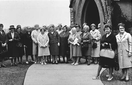 Photograph of twenty one middle-aged women in overcoats and hats standing in a group outside the west door of a church; they have been identified as members of the Mothers' Union in Thornley
