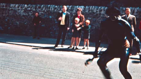 Photograph showing a group of a man, woman and two children, and two other men watching a blurred figure in the forefront of the picture; the photograph has been identified as Carnival, Thornley