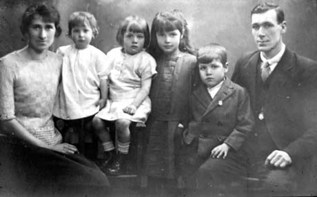 Photograph showing a young woman on the left of the picture wearing a skirt and silk jumper; next to her are a small child aged approximately two years, a child aged approximately three years, a girl aged approximately six years and a boy aged approximately five years; on the right of the picture is a young man wearing a suit and tie; they have been identified as Phil and Frances Rutherford and Family of Thornley
