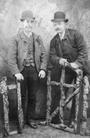Photograph showing two men dressed in suits, ties, and bowler hats, leaning on artificial rustic gates in a photographer's studio; they have been identified as Mr. Coxon, a sinker, standing on the right of the picture, with a friend