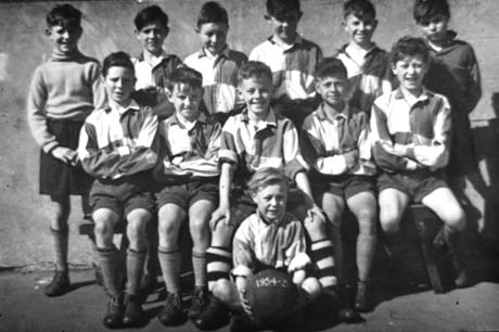Photograph of twelve boys, aged approximately ten years, wearing football strip posed against a wall; a boy at the front of the group is holding a football with the figures 1954-55 on it; they have been identified as members of a school football team in Thornley