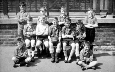 Photograph showing twelve boys aged approximately ten years posed in front of a raised walkway; they are wearing football boots and one of the boys is holding a football on which the figures 1939-40 are written; they have been identified as Junior Football Team, Thornley