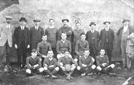 Photograph showing eleven men in football strip, with six other men in suits, posed against a wall; a man at the front of the group is holding a football on which the words Thornley Officials A[thletic] F[ootball] C[lub] is written; the date on the football is difficult to discern, but the date has been given as 1920
