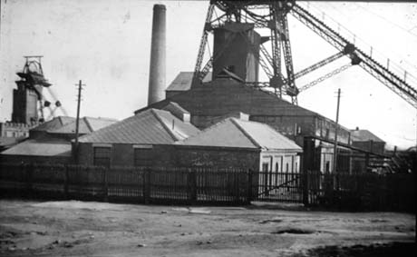 Photograph showing on the left of the picture in the distance the winding gear of a colliery; in the middle and foreground of the picture are low buildings of a colliery with a chimney behind them; above these buildings the bottom of what appears to be further winding gear can be seen; the colliery has been identified as Thornley Colliery