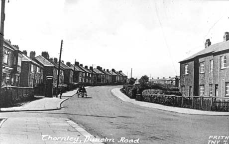Postcard photograph entitled Thornley, Dunelm Road Frith TNY , showing a road running away from the camera, uphill, curving round to the right; on the left of the road, semi-detached houses can be seen; a telephone box can be seen and a horse and cart is being driven away from the camera; on the right of the picture terraced houses can be seen in the distance and the facade of three terraced houses in the foreground