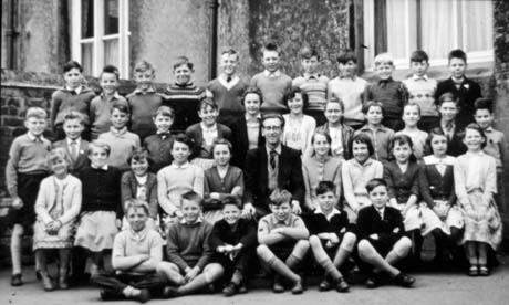 Photograph showing thirty nine children, aged approximately nine years, posed in the angle between a garden wall and the wall of a building; sitting in the middle of the group is a man, identified as Mr. Willans, the children's teacher; a child, described as End Back, has been identified as Michael Foster