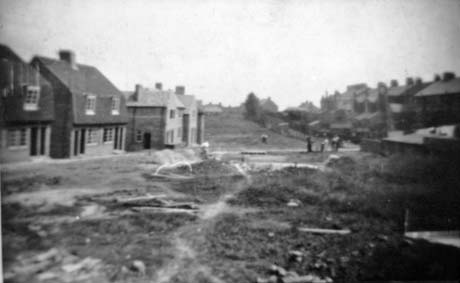Photograph showing, on the left of the picture, the exterior of three detached houses; in the centre of the picture is open ground; on the right of the picture are indistinct buildings; the photograph has been identified as Gore Hall, Thornley