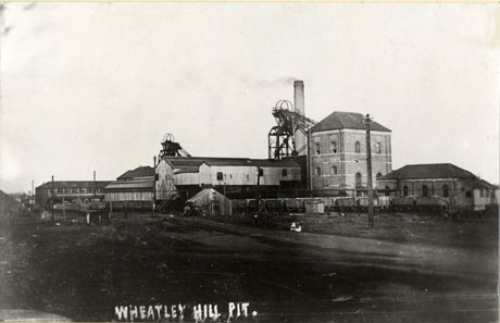 Postcard photograph entitled Wheatley Hill Pit, showing the buildings, winding house, a chimney and two winding gear of the colliery; coal waggons can be seen on the right of the picture
