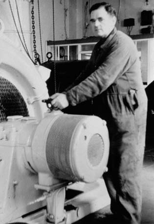 Photograph showing a man a standing at the right of the picture, bending to touch a large machine, which takes up the left-hand part of the photograph; he has been identified as Tommy Mason at Power Station