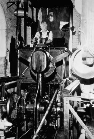 Photograph showing a man wearing overalls sitting at the back of the picture high up at the controls of a large machine; he has been identified as Bob Blacklock at No. 2 Controls, Wheatley Hill