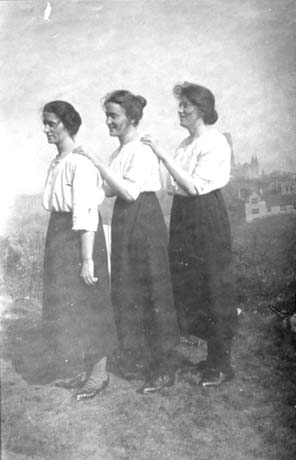 Photograph showing three young women standing sideways to the camera with their left arms resting on the shoulders of the woman in front; they are all wearing light-coloured blouses and ankle-length dark skirts; they have been identified as Peter Lee's Three Daughters, Edith, Alice and Maud at Durham