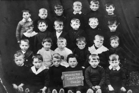 Photograph of a group of twenty four boys, aged approximately five years; a boy on the front row is holding a slate which reads: Wheatley Hill Infants' School Class 1(c)
