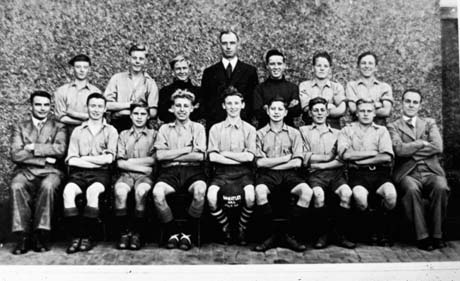 Photograph showing thirteen boys, aged approximately fourteen years, in football strip, posed against a wall, accompanied by three men; a boy on the front row is holding a ball on which only the words Wheatley Hill can be discerned; it is likely that the team is a school team