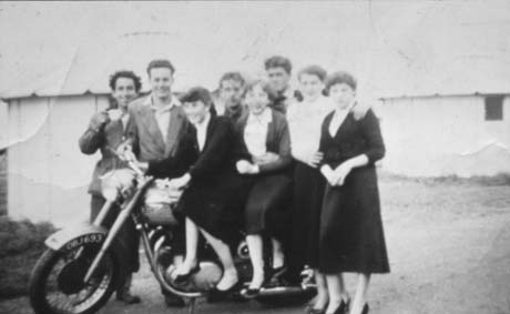 Photograph showing a group of six young men and three young women posed on and round a motor cycle, the registration number of which is as follows: OBJ 693; behind the group is the exterior of a marquee; the men are dressed in jackets and open-necked shirts and the women in skirts and cardigans; the photograph has been identified as Holiday at Hart Wheatley Hill