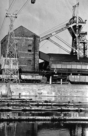 Photograph showing at the front of the photograph a stretch of water across which pipes are laid; beyond the water the winding house and the winding gear of a colliery can be seen; the photograph has been identified as No. 2 Winder and Headgear, Wheatley Hill
