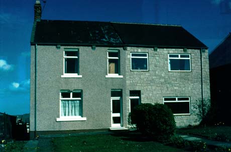 Photograph of the front of two semi-detached houses with one window on the ground floor and two on the first floor; one appears to have retained the original shape of the windows and the other has had differently shaped windows installed and a cladding of stone put on the walls; the photograph has been identified as Home of Peter Lee Before Moving to Durham in Wheatley Hill