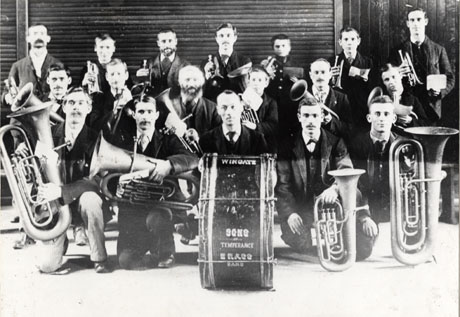 Photograph showing nineteen men kneeling and standing holding musical instruments; at the front of the group is a drum with the following words on it: Wingate Sons of Temperance Brass Band