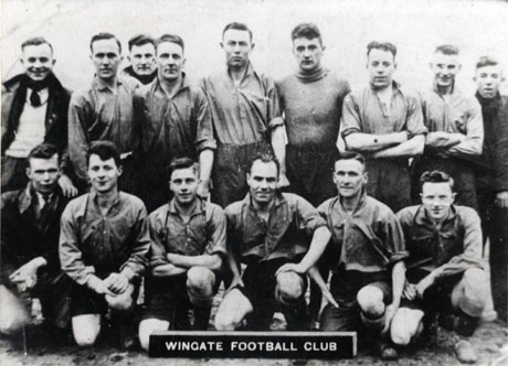Photograph of eleven men in football strip with four other men in suits and overcoats; in front of them is a sign reading: Wingate Football Club