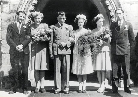 Photograph showing a newly-married bride and groom standing outside the west door of a church; they are accompanied by two women and two men; all three women are wearing suits and carrying bouquets of flowers and fern; the men are dressed in lounge suits and have flowers in their button holes;no other people are present; the picture has been identified as Wilf Foster's Wedding, Wingate