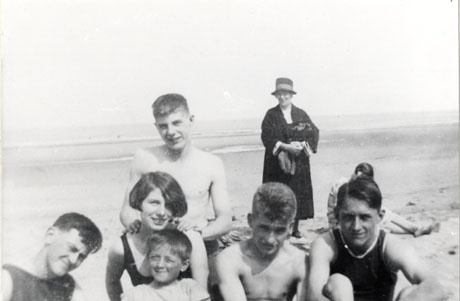 Photograph looking towards the sea with a middle-aged woman dressed in a dark coat and hat standing behind a group of five boys and one girl, whose head and shoulders only can be seen; the girl aged approximately fifteen years is wearing a bathing costume; two boys aged approximately the same age are bare-chested and two others are wearing singlets; a small boy, aged approximately seven years, is at the front of the group wearing a short-sleeved shirt; they have been identified as Little Jimmy Russell and Gordon Russell (right) of Wingate