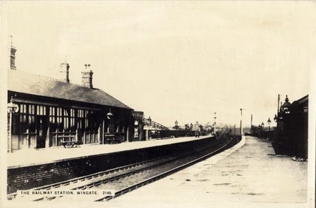 Postcard photograph entitled The Railway Station, Wingate. 2149, showing the line curving away into the distance and two platforms; the buildings on the platform at the left only can be seen along with seats and gas lights