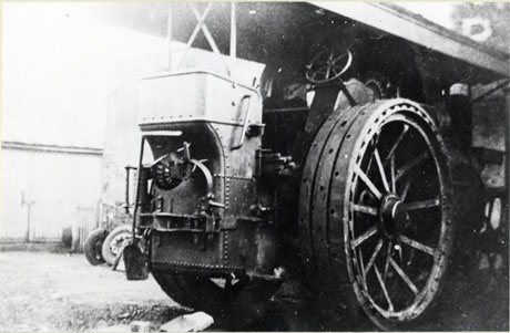 Photograph showing a close-up view of a wheel, steering wheel and seat for the operator of an engine which has been identified as Murphy's Showground Engine, Wingate; it is possible that the engine is a steam engine