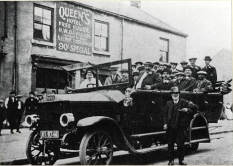 Photograph showing approximately twenty five men sitting in a motor charabanc outside a public house on which the following is written: Queen's Hotel Free House R. W. Davison Licensee .... Ales Wines .... 90 Shilling Special; the charabanc has the registration MX 9748; four people are on the pavement behind the car watching and an elderly man is standing in front of the charabanc; the Queen's Hotel has been identified as being in Wingate