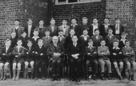 Photograph of twenty nine boys, aged approximately twelve years, grouped against the wall of a building; two men are sitting in the middle of the front row; they have been identified as a School Group in Wingate