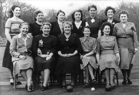 Photograph showing twelve women grouped in the open air with a bowling ball and a jack at their feet; they are dressed in suits, dresses, and skirts and jumpers; they have been identified as Ladies Bowling Club, Wingate