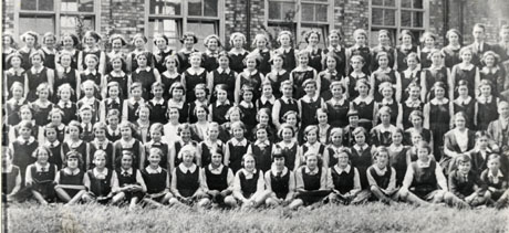 Photograph showing one hundred and ten girls and school mistresses, posed outside buildings identified as those of the A. J. Dawson Grammar School; the photograph adjoins wing0134 on the right and wing0136 on the left
